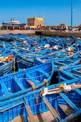 Eine Flotte blauer Fischerboote drängt sich im Hafen von Essaouira in Marokko zusammen. Sie können auch die Befestigungsanlagen und einen Turm der Zitadelle von Mogador sehen © Louis-Michel DESERT