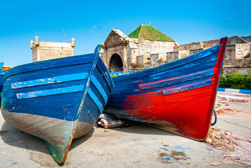 a blue and a red and blue fishing boats are stranded on a dock at the foot of the citadel of...