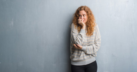 Fototapeta premium Young redhead woman over grey grunge wall looking stressed and nervous with hands on mouth biting nails. Anxiety problem.