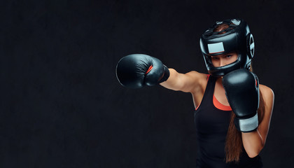 Sportive woman in sportswear wearing a protective helmet and boxing gloves, training in gym....