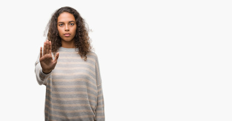 Beautiful young hispanic woman wearing stripes sweater doing stop sing with palm of the hand. Warning expression with negative and serious gesture on the face.