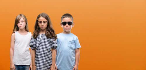 Group of boy and girls kids over orange background with a confident expression on smart face thinking serious