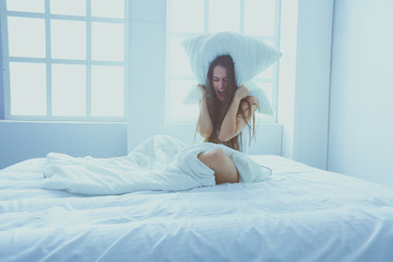 Young caucasian woman covering her head and ears with pillows.