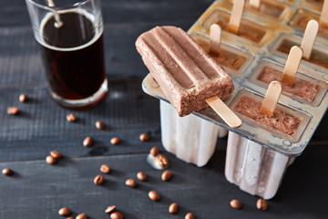 A glass of cold coffee and a coffee sorbet on a stick on a black wooden table. Top view