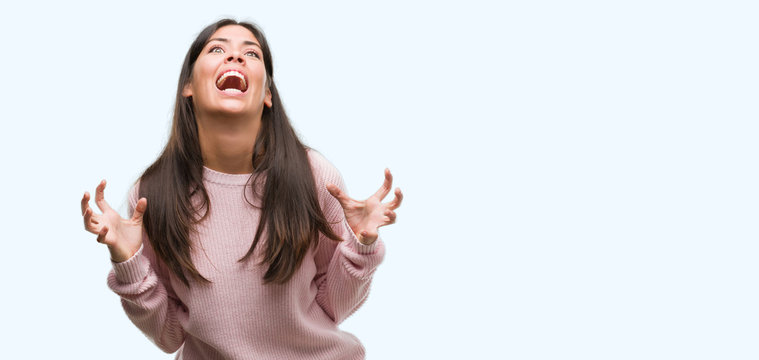 Young beautiful hispanic woman wearing a sweater crazy and mad shouting and yelling with aggressive expression and arms raised. Frustration concept.