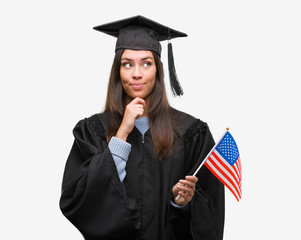 Young hispanic woman wearing graduated uniform holding flag of america serious face thinking about question, very confused idea