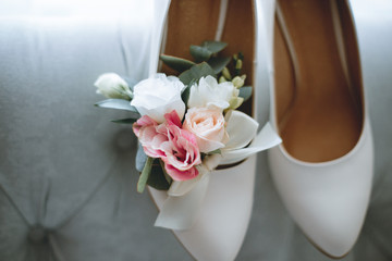 Brides wedding shoes with a bouquet with roses and other flowers on tha arm chair