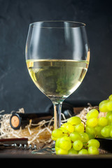 White wineglass and white yellow green bunches of berry grapes with bottle