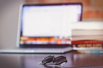 sunglasses on a table with laptop computer and books on brick wall background