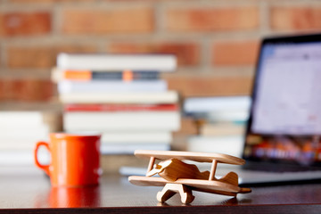 Wooden airplane toy on a table with books and laptop computer on brick wall background