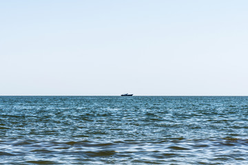Obraz premium blue sea with waves, far away on a horizon line floating ship, nature abstract background