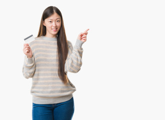 Young Chinese woman over isolated background holding credit card very happy pointing with hand and finger to the side