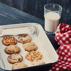 Homemade oatmeal biscuits on a baking sheet with glass of milk for Santa Claus on a black wooden table.