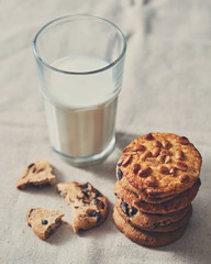 The glass of milk with a stack of cookies with chocolate chunks and peanut on a textile towel background,