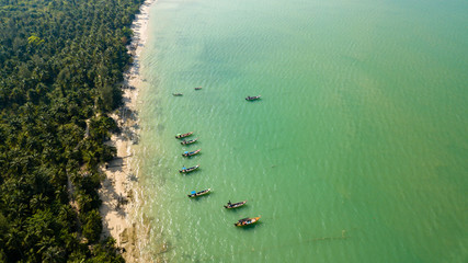 Aerial drone view of colorful traditional Longtail boats at anchor off a sandy beach in Thailand