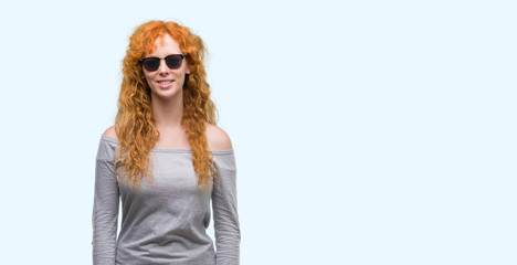 Young redhead woman wearing sunglasses with a happy face standing and smiling with a confident smile showing teeth