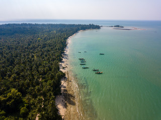 Traditional Longtail boats anchored off a long sandy beach in Thailand