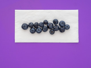 Healthy superfood blueberries on white paper napkin, serviette, on purple background. With copyspace.