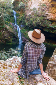 Back view of young girl in straw hat and looking at waterfall. Caucasian young lady looks at falling water, photo on fresh air. youth adolesce in wild nature