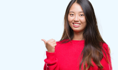 Young asian woman wearing winter sweater over isolated background smiling with happy face looking and pointing to the side with thumb up.