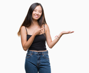 Young asian woman over isolated background amazed and smiling to the camera while presenting with hand and pointing with finger.