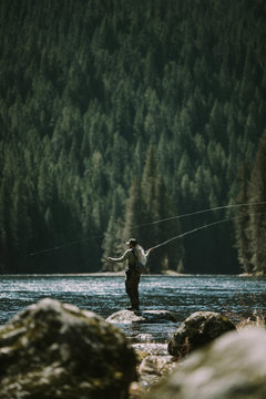 Man fly fishing in a river with mountains and forest