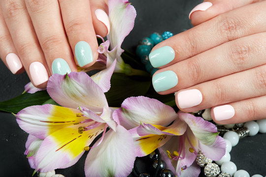 Hands with short manicured nails colored with pink and green nail polish and lily flowers