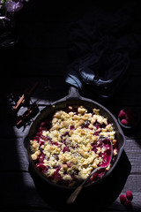 Crumble pie with berries on wooden background.