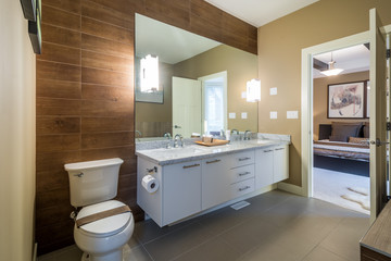 Interior design of a luxury bathroom with a wood wall and a large mirror, overlooking a bedroom.