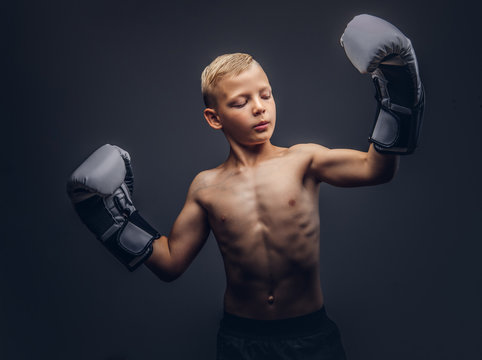 Young shirtless boy boxer with boxing gloves posing in a studio.