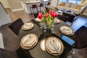 Modern round dining room table set for dinner in a luxury  house, with a kitchen in the background. Interior design.