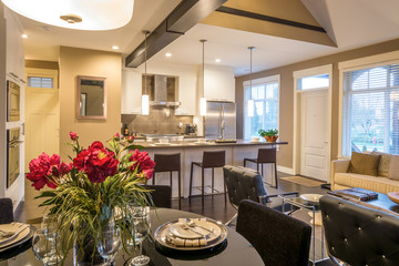 Modern round dining room table set for dinner in a luxury  house, with a kitchen in the background. Interior design.