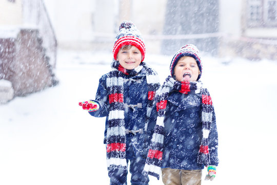 Two little kid boys in colorful fashion clothes playing outdoors during strong snowfall. Active leisure with children in winter on cold days. Happy siblings and twins having fun with first snow.