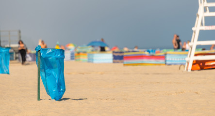 An empty garbage bag on the beach on a sunny summer day, in the background people, a beach screen and a lifeguard stand.