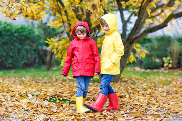 Two little best friends and kids boys autumn park in colorful clothes. Happy siblings children having fun in red and yellow rain coats and rubber boots. Family playing outdoors. active leisure.