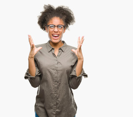 Young afro american woman wearing glasses over isolated background crazy and mad shouting and yelling with aggressive expression and arms raised. Frustration concept.