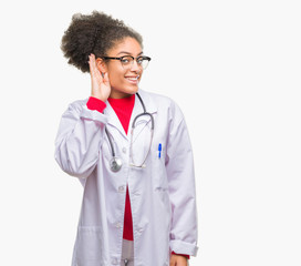 Fototapeta premium Young afro american doctor woman over isolated background smiling with hand over ear listening an hearing to rumor or gossip. Deafness concept.