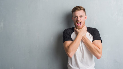 Young redhead man over grey grunge wall shouting and suffocate because painful strangle. Health problem. Asphyxiate and suicide concept.