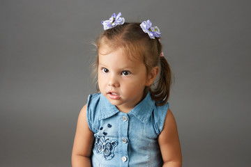 Happy face funny child girl in a blue dress. Portrait of adorable smiling little cute girl child with bow on her head isolated on gray background with copy space.