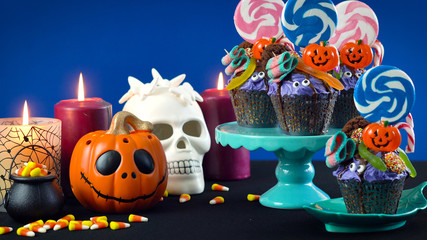 Happy Halloween candyland drip cake style cupcakes with lollipops and candy on blue background.