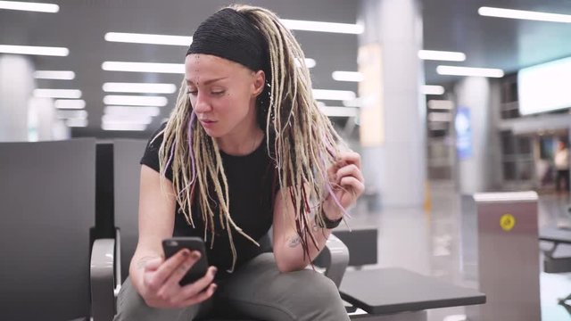 Attractive young woman blogger with dreadlocks using phone at the airport. Portrait of beautiful hipster woman