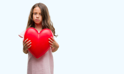 Brunette hispanic girl holding red heart with a confident expression on smart face thinking serious
