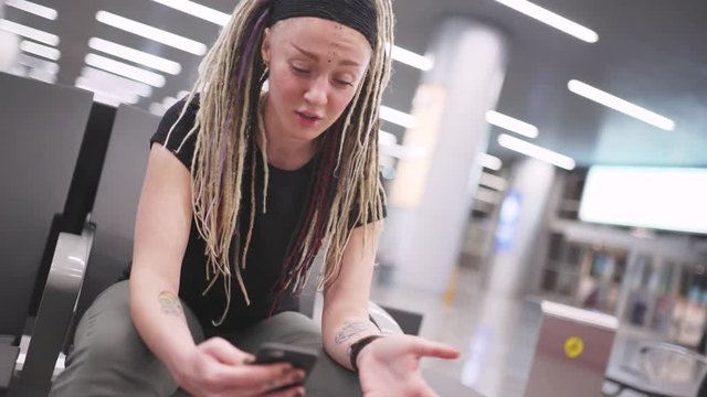 Attractive young woman blogger with dreadlocks using phone at the airport. Portrait of beautiful hipster woman