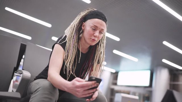 Attractive young woman blogger with dreadlocks using phone at the airport. Portrait of beautiful hipster woman