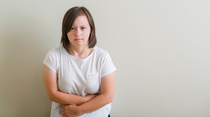 Down syndrome woman standing over wall with hand on stomach because nausea, painful disease feeling...
