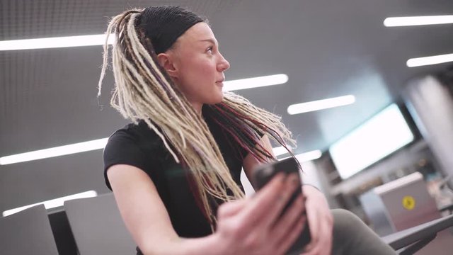 Attractive young woman blogger with dreadlocks using phone at the airport. Portrait of beautiful hipster woman