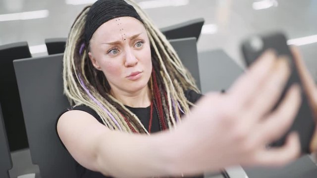 Attractive young woman blogger with dreadlocks using phone at the airport. Portrait of beautiful hipster woman