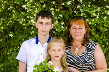 
Mom and two children of teenagers are standing by the bush of jasmine.