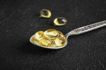 Spoon with cod liver oil pills on table, closeup