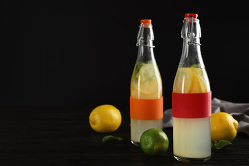 Bottles with natural lemonade on table against dark background